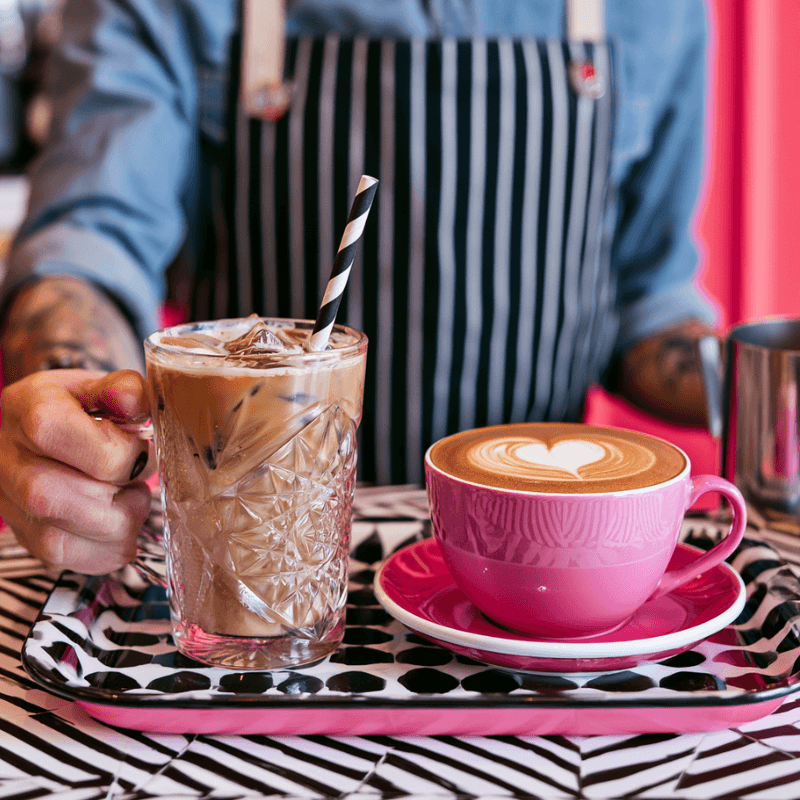 Barista servant une iced horchata de chufa et un café crème art en tasse rose, format professionnel coffee shop